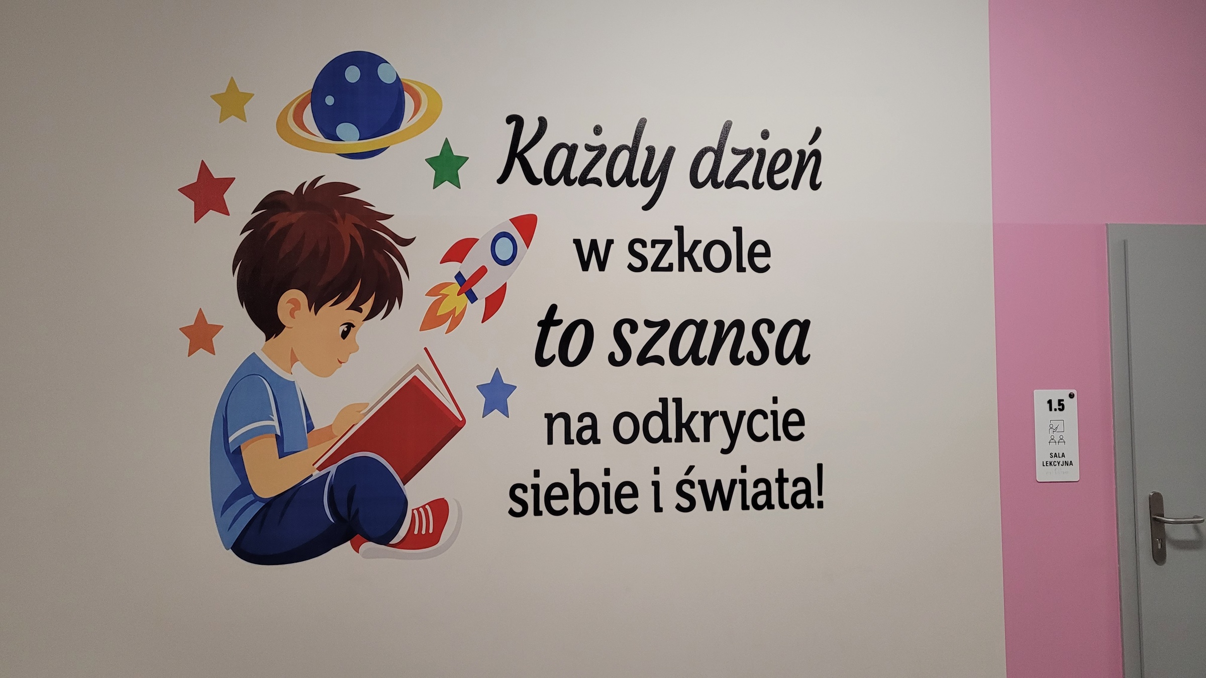 Książka i kosmos — Szkoła Podstawowa w Kłoczewie Czytający chłopiec, rakieta, planeta i gwiazdy obok napisu o odkrywaniu siebie i świata na szkolnej ścianie.