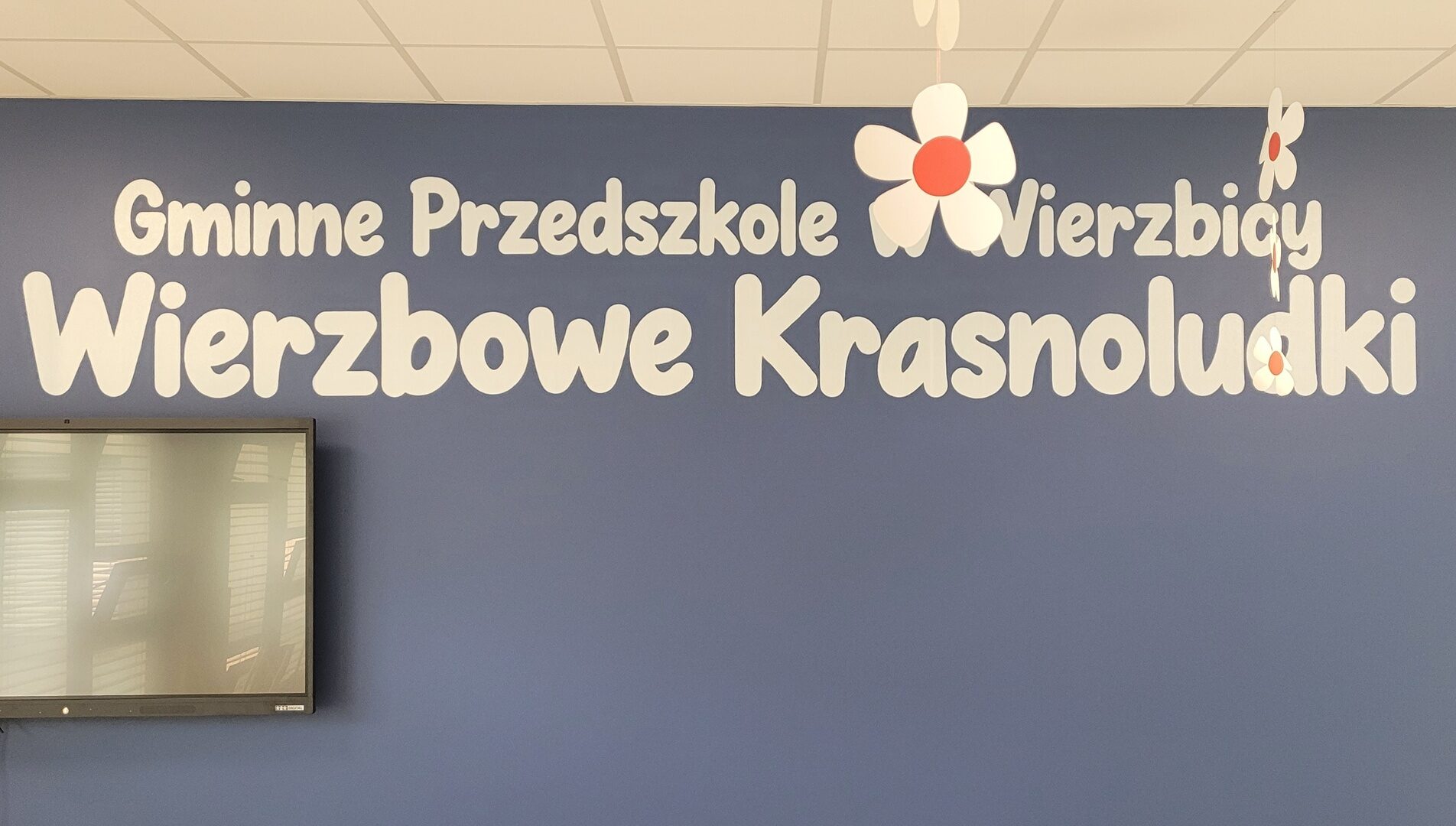 Wierzbowe Krasnoludki — Wierzbica, napis w sali przedszkola Jasny napis Gminne Przedszkole w Wierzbicy Wierzbowe Krasnoludki na granatowej ścianie.
